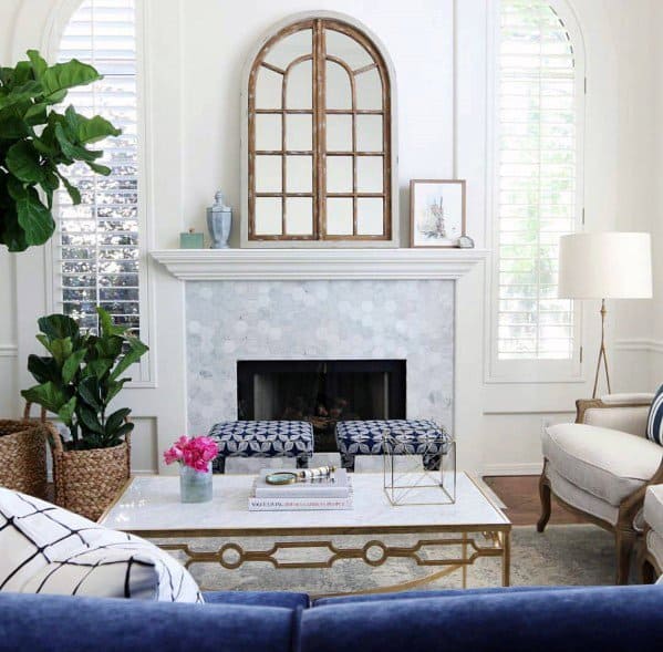 Elegant living room with white hexagon-tiled fireplace, mirror decor, blue patterned ottomans, and armchairs.