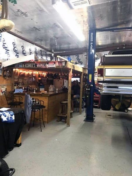 Rustic garage bar with wooden structure, string lights, and adjacent vehicle lift area.