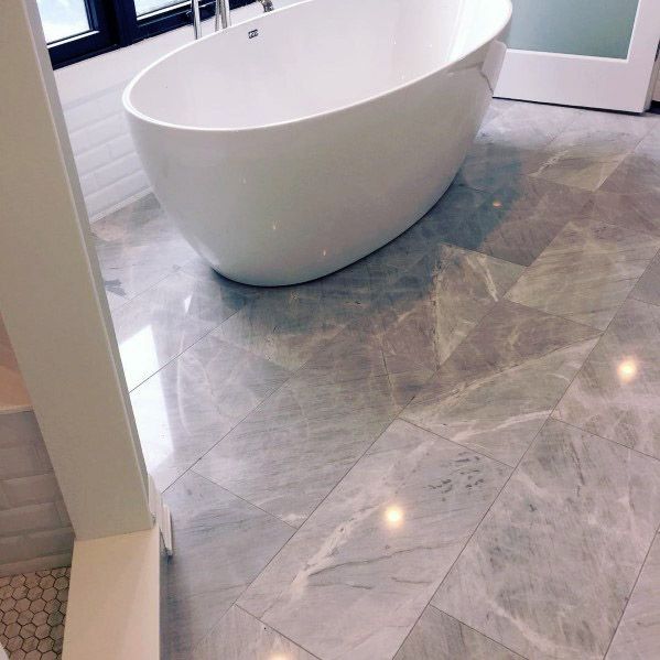 A modern bathroom with a grey freestanding bathtub and marble tile floor