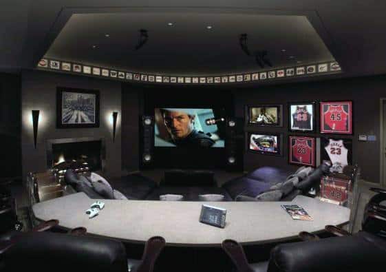 Home theater with curved seating, multiple screens, sports memorabilia, and dim lighting.