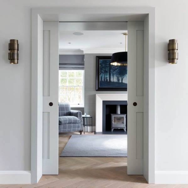 Stylish white double pocket doors with recessed panels, opening into a cozy living room with modern design elements, including a fireplace and soft neutral tones