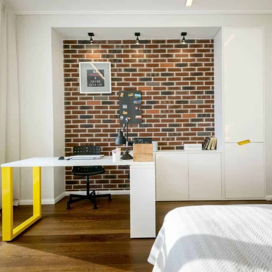 Modern bedroom with white desk, yellow accent, and brick wallpaper feature wall.