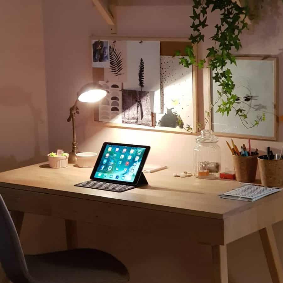 Wooden desk with tablet, plant decor, and artwork in a cozy bedroom workspace.