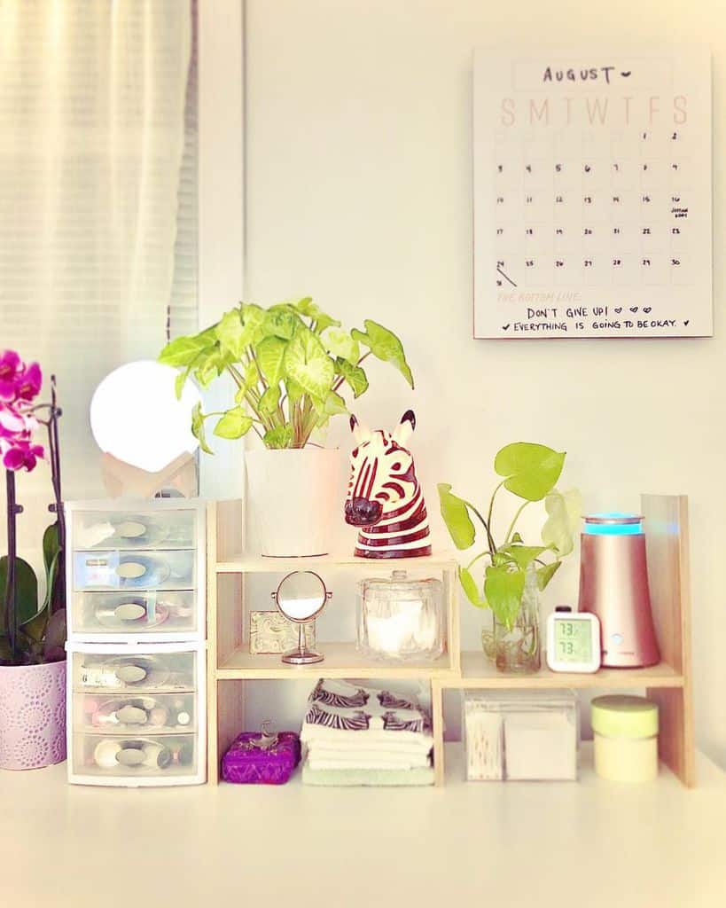 Organized vanity with plants, storage drawers, and calendar on bedroom wall.