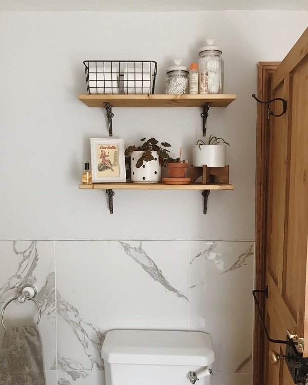 Bathroom with wooden shelves, marble wall tiles, and potted plants for a minimalist look.