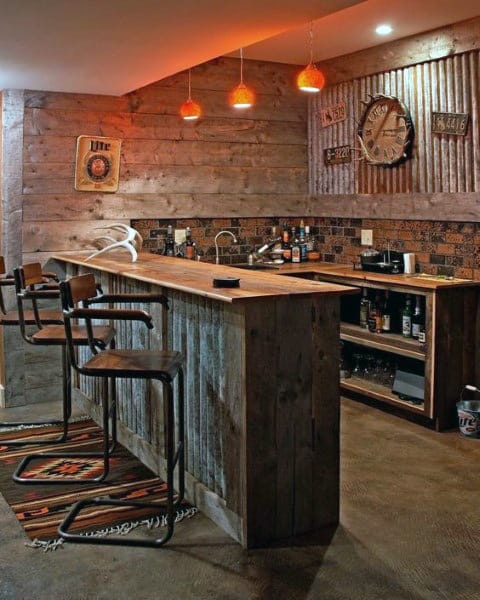 Rustic home bar with wooden panels, industrial stools, warm lighting, and vintage wall decor.