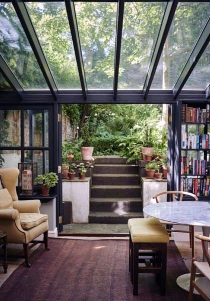 Sunroom with glass ceiling, cozy vintage seating, and a lush garden view.