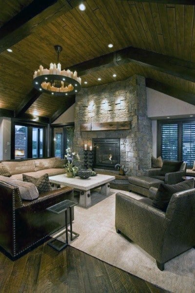 Cozy vintage rustic living room with a large stone fireplace, vaulted wooden ceilings, and comfortable furniture in neutral tones