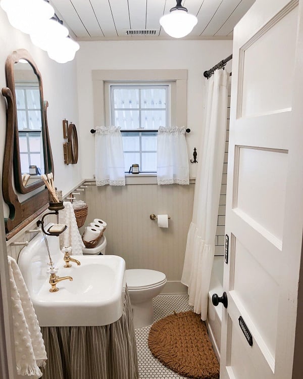 Cozy farmhouse vintage bathroom with a sink, toilet, bathtub, and window adorned with lace curtains