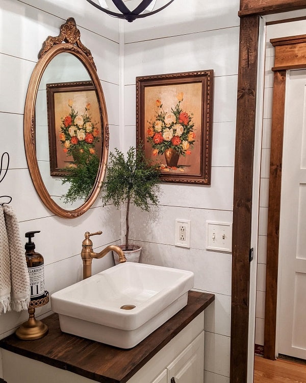 Rustic bathroom with ornate mirror, vessel sink, and framed flower painting on wood vanity.