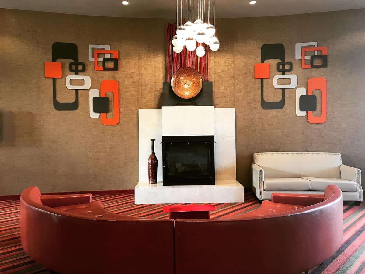 Modern lounge with red, white, and brown decor, abstract wall art, circular seating, fireplace, and hanging lights