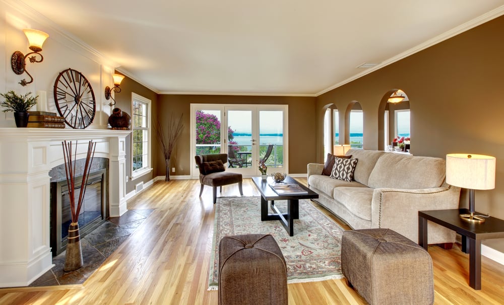 A warm living room with a brown plush sofa, fireplace, coffee table, and ocean view through glass doors