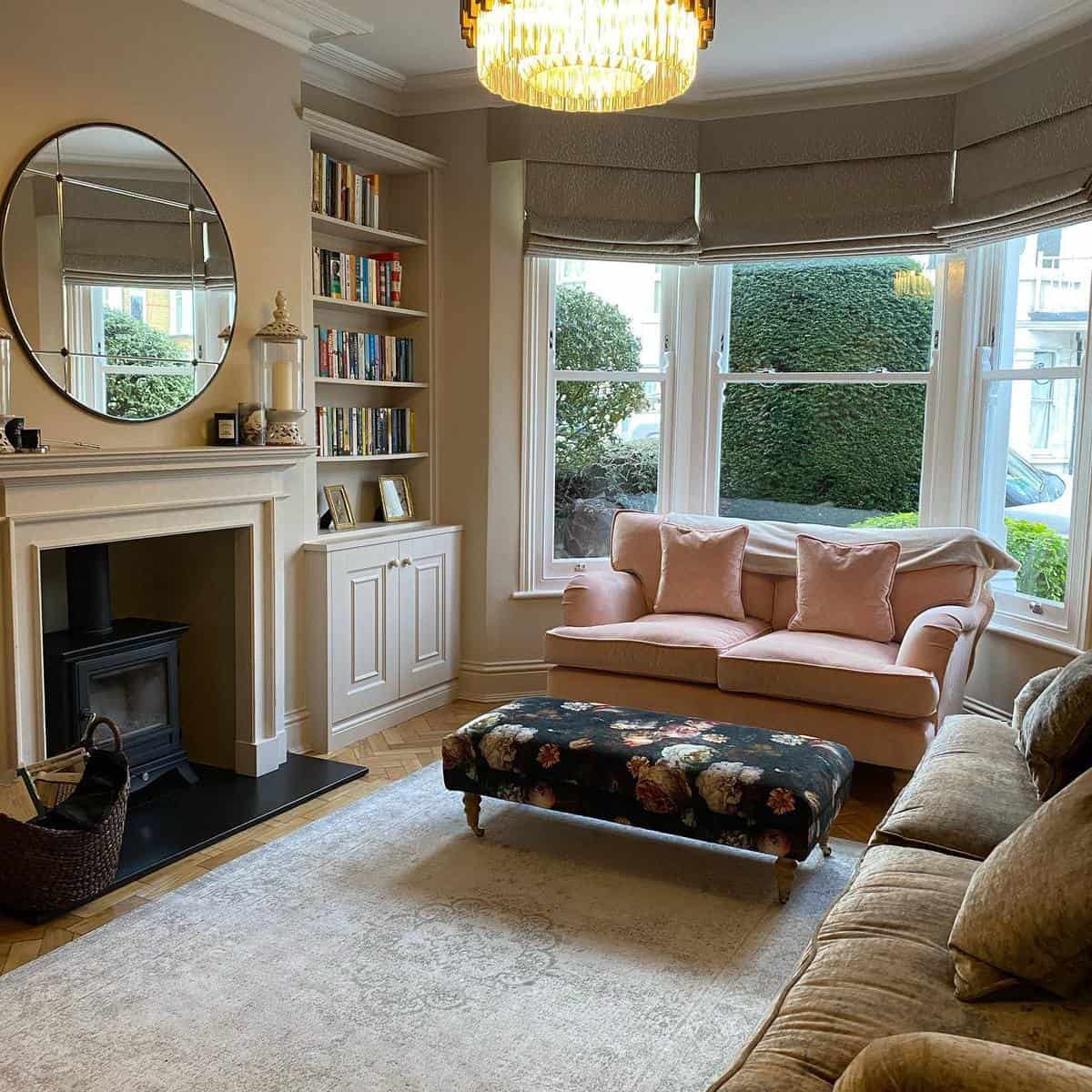 Cozy living room with a brown fireplace, sofas, a floral ottoman, and a large window with garden view