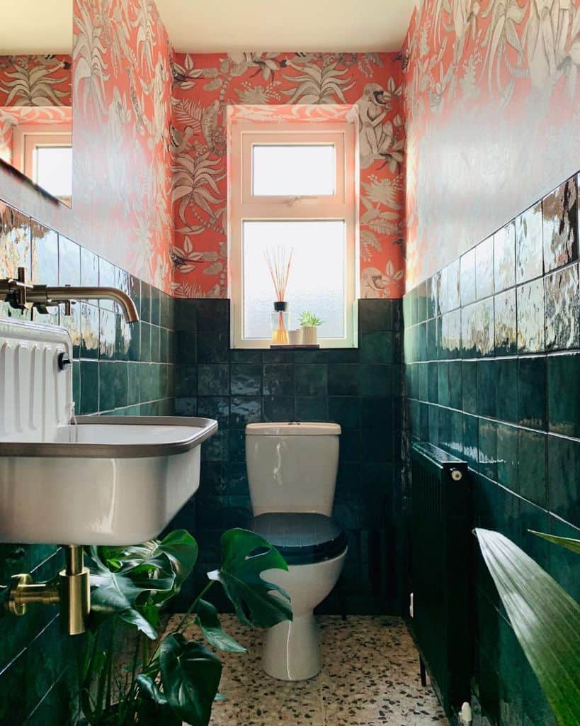 A vibrant bathroom features floral wallpaper, dark green tiles, and a white sink and toilet with a plant on the floor