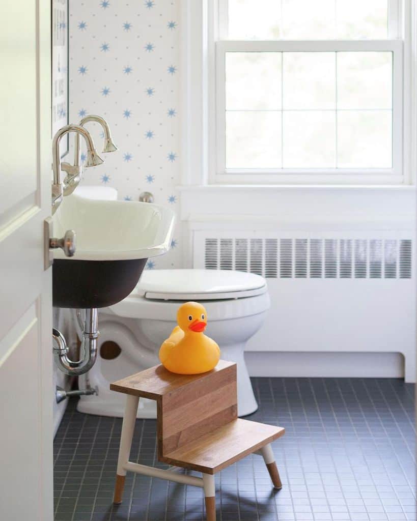 Bathroom with a sink, toilet, and a wooden step stool featuring a rubber duck under a window with natural light