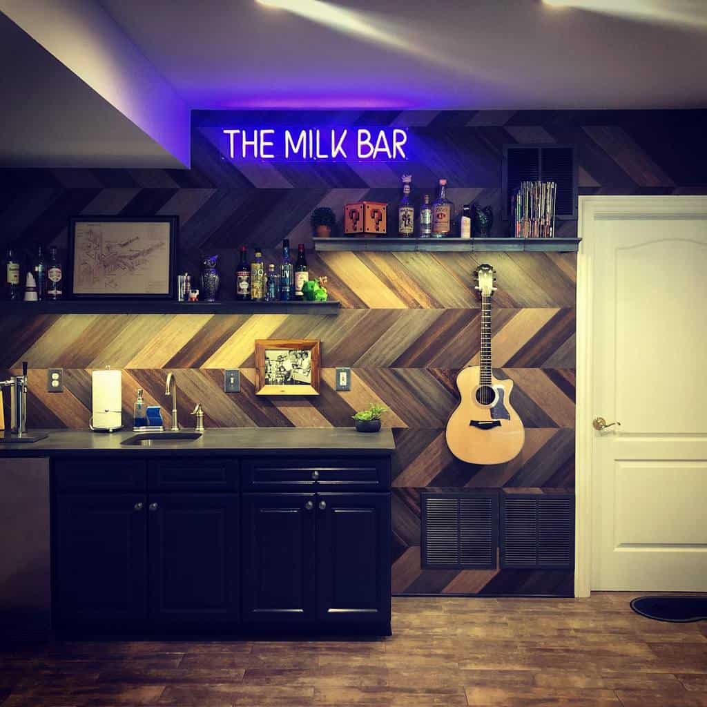 A unique wet bar featuring dark cabinets, a herringbone wood accent wall, floating shelves, and a custom neon sign for a personalized touch.