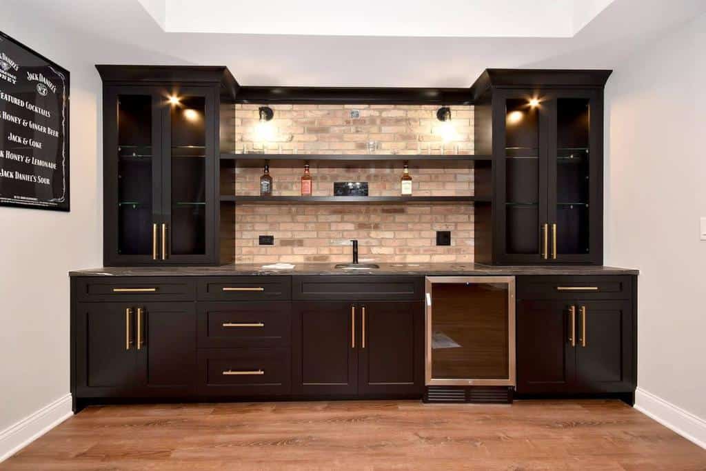 Modern black wet bar with gold accents, brick backsplash, and built-in cooler.