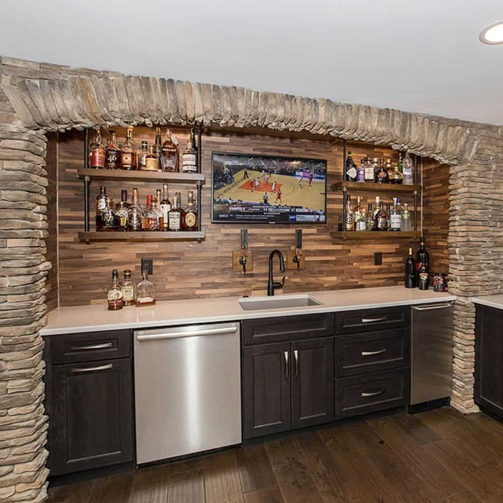 Rustic wet bar with stone arch, wood backsplash, open shelving, and built-in beer taps.