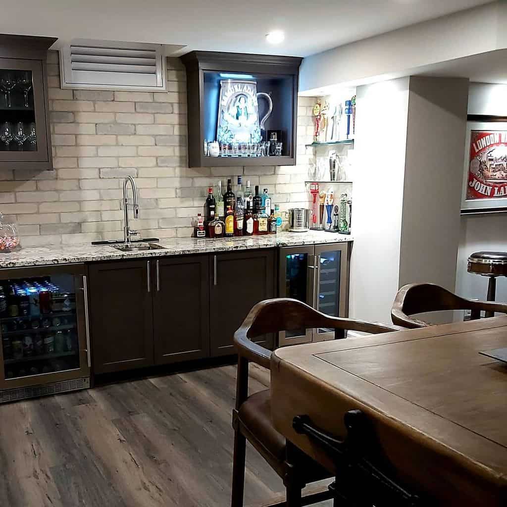 Modern basement wet bar with dark cabinetry, brick backsplash, granite countertop, and beverage coolers.