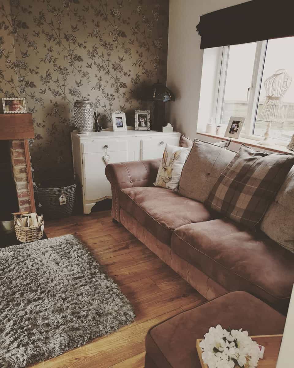 Cozy living room with a brown sofa, floral wallpaper, and white cabinet. A gray rug adorns the brown wooden floor