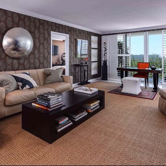 Modern living room with tan and brown sofas, a dark coffee table, wall art, and an office area near large windows