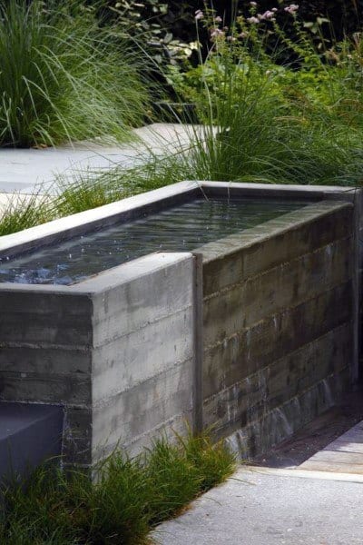 Modern raised concrete pond with minimalist design, surrounded by tall grasses and garden landscaping.