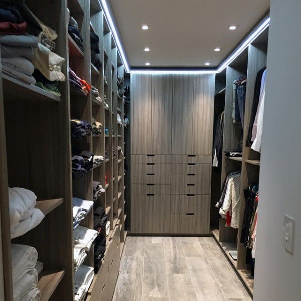 Walk-in closet with shelves of folded clothes and hanging garments, featuring wooden flooring and ceiling lights