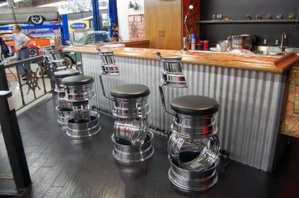 Industrial garage bar with corrugated metal counter, wooden top, and stools made from car wheels.