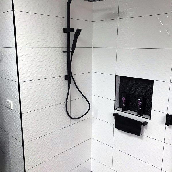 White textured shower tiles with black handheld showerhead and recessed shelf.