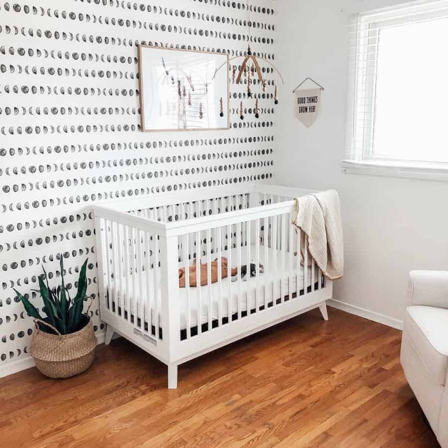 White baby room with moon phase feature wall, white crib, and woven basket plant.