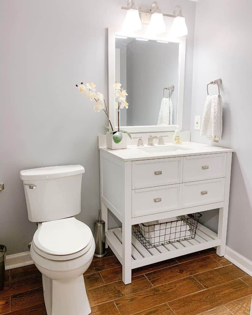 A white bathroom featuring an old-style cabinet, a wooden floor, and simple decor, giving a clean and classic feel.