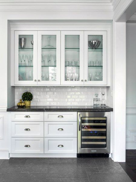 Sleek white mini bar with glass-front cabinets, a wine cooler, and subway tile backsplash.