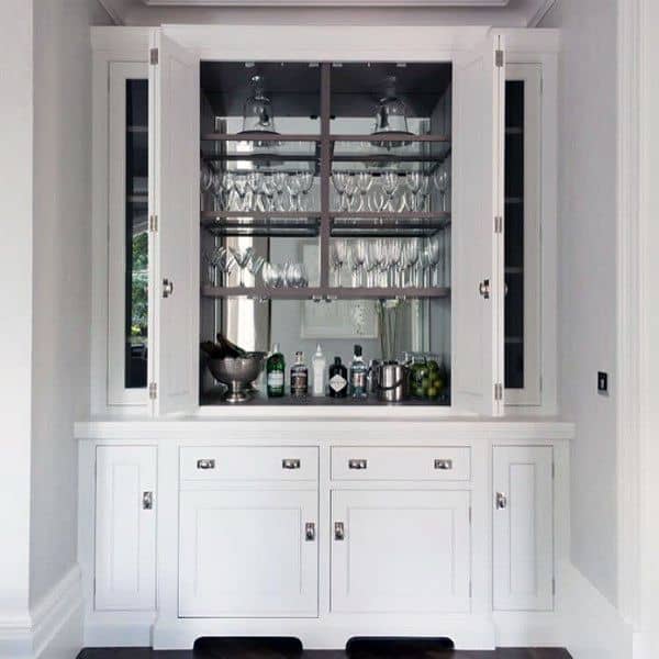 Elegant mini bar with white cabinets, mirrored backsplash, glassware shelves, and chrome accents.