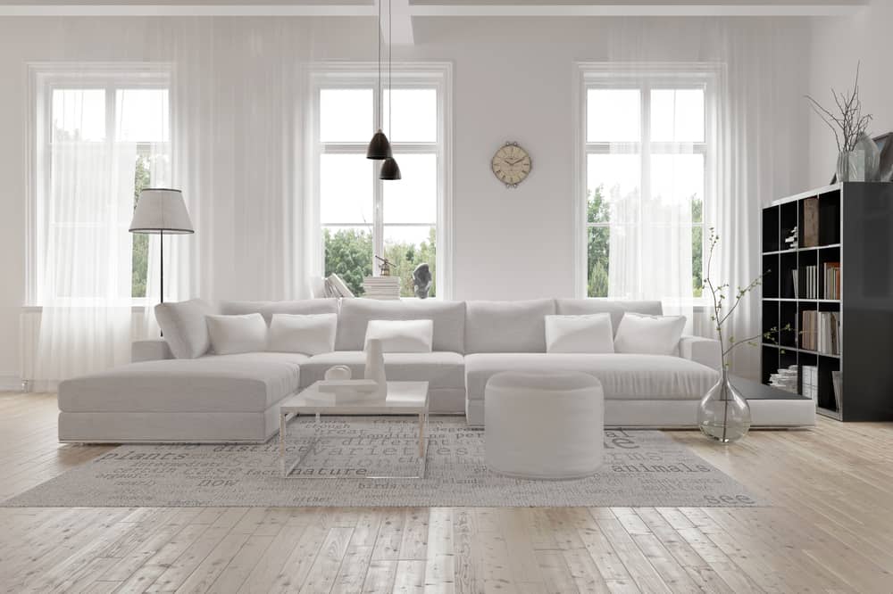 Cozy minimalist living room featuring a white sectional sofa, light wood floors, and a soft ambiance with natural light streaming in