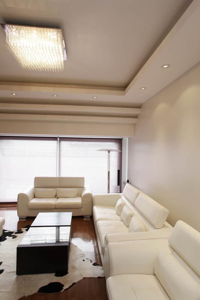 Luxurious white living room with leather sofas, a crystal chandelier, cowhide rug, and sleek modern accents