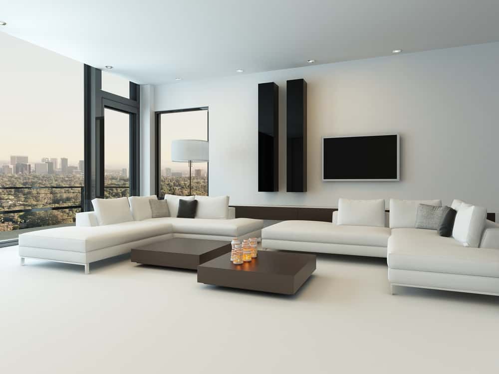 Spacious minimalist living room with a white sectional sofa, panoramic city views, and sleek black accents