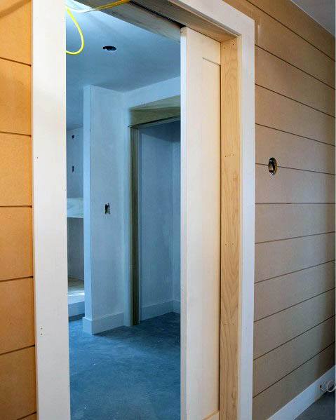 Simple, unfinished pocket door frame with natural wood edges and a white interior door, set within a warm shiplap-paneled wall, giving a modern farmhouse vibe