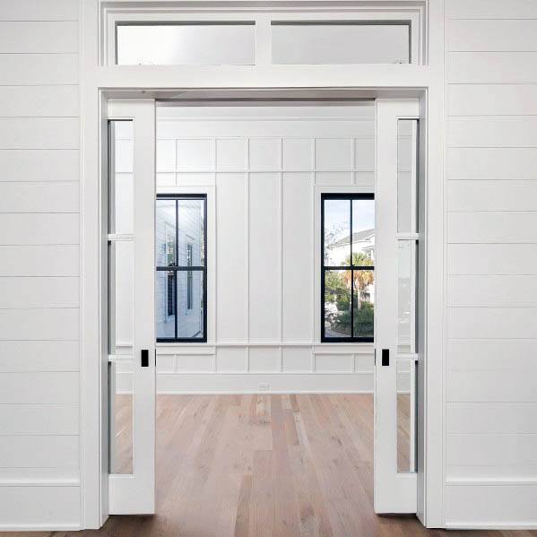 Elegant double white pocket doors with glass panels, framed by detailed molding and a transom window above.