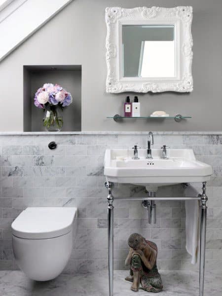 Elegant half bath with a white sink, toilet, mirror, floral arrangement, and decorative statue under the sink