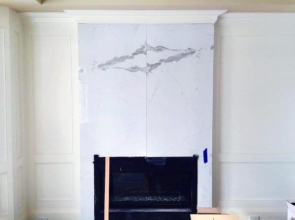 Modern fireplace with large white marble tiles featuring gray veining and a black hearth.