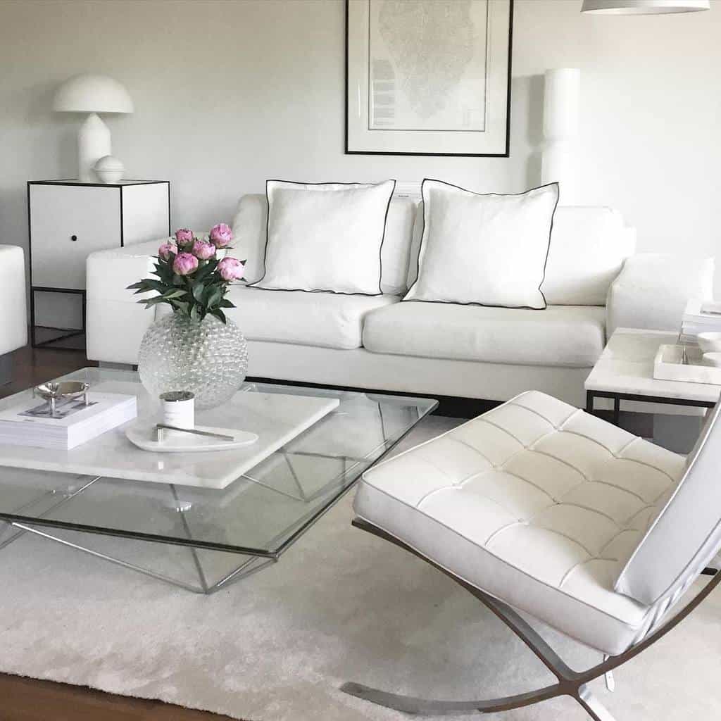 Elegant white minimalist living room with a glass coffee table, tufted chair, and floral accents.