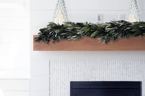 A clean white mosaic-tiled fireplace complemented by a wooden mantel and seasonal greenery.