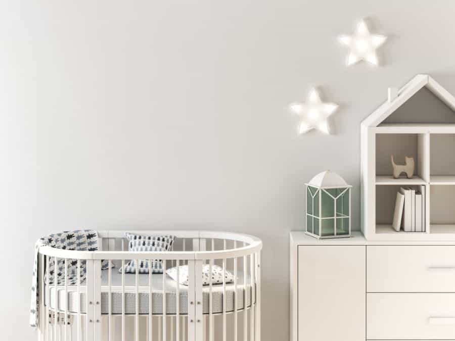 Minimalist baby room with a round white crib, star-shaped wall lights, and house-shaped shelf decor.