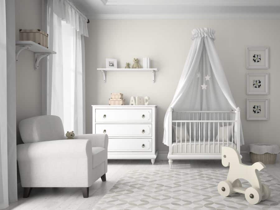 White baby room with canopy crib, armchair, dresser, and wooden rocking horse on patterned rug.