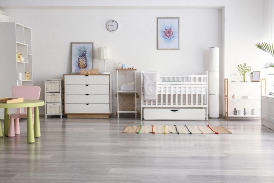 Minimalist modern nursery with white crib, dresser, and pastel kids' table on wooden floor.