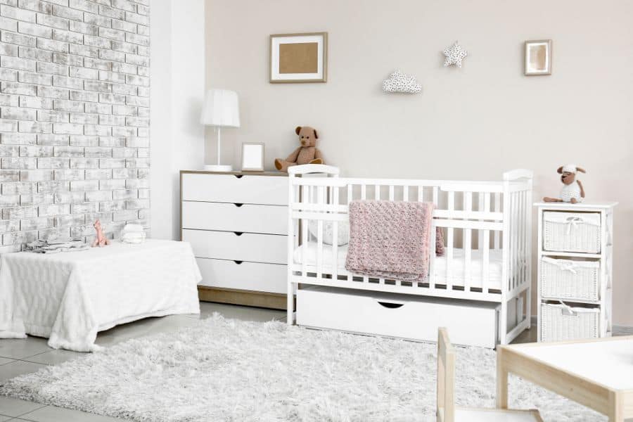 Nursery with white furniture, exposed brick feature wall, and soft textured rug.