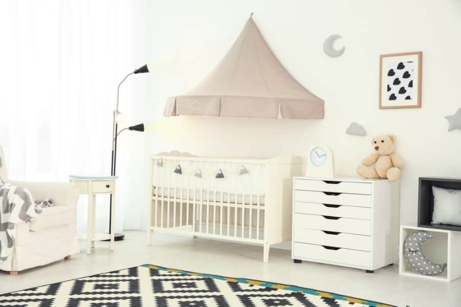 Neutral baby room with a canopy crib, moon and cloud decor, and geometric patterned rug.