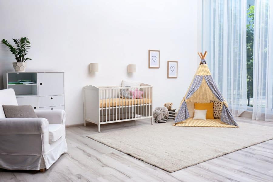 Spacious baby room with a white crib, cozy tipi tent, soft beige rug, and natural light from large windows.