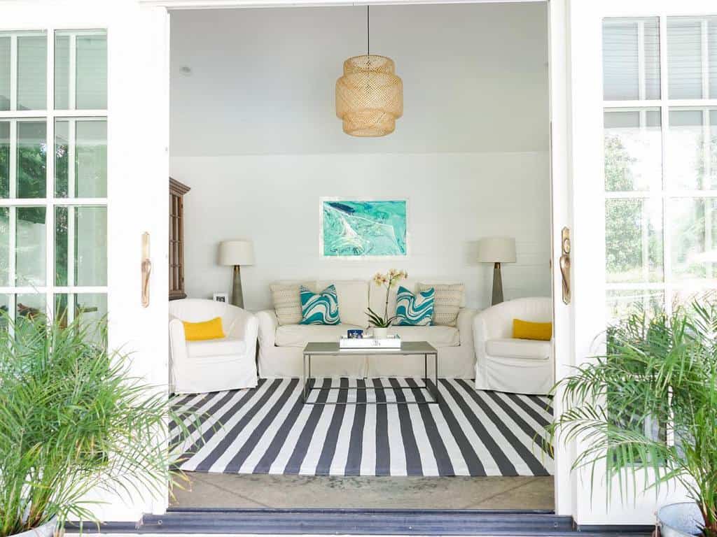 Bright sunroom with white furniture, striped rug, green plants, and coastal-inspired decor.