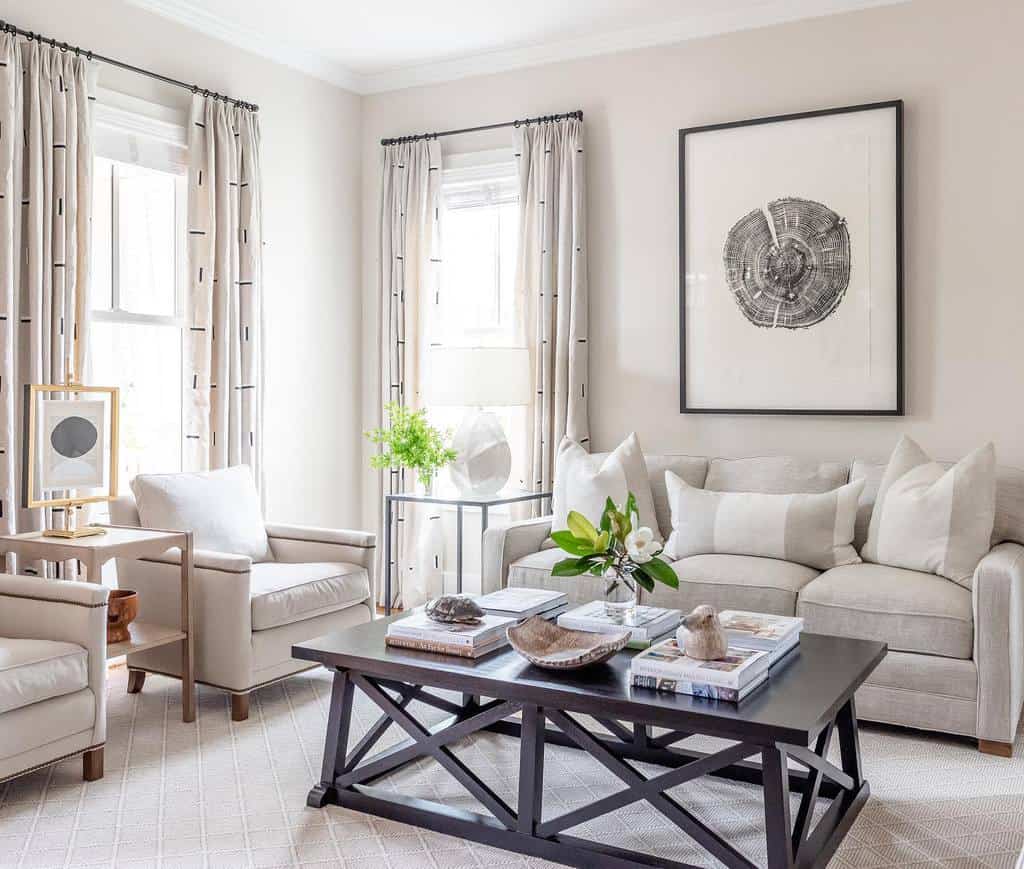 Modern sunroom with neutral sofa, cozy armchairs, black coffee table, and framed artwork.